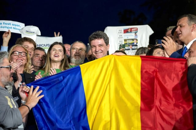 Presidential candidate Nicuşor Dan, center, poses behind a Romanian flag after polls closed in the May 18 presidential election.