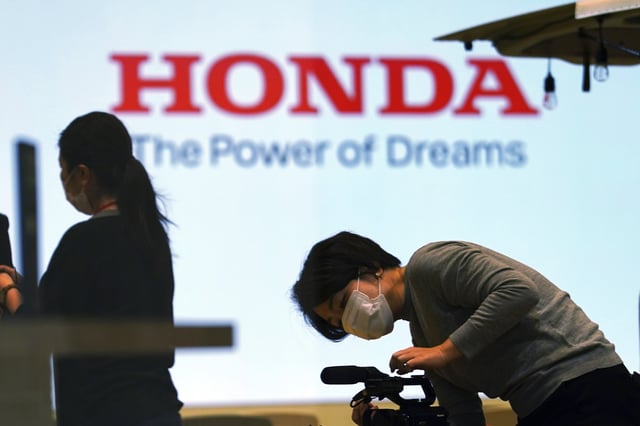 FILE - A woman wearing a protective mask to help curb the spread of the coronavirus works near the logo of Honda Motor Company at a showroom on May 13, 2021, in Tokyo. (AP Photo/Eugene Hoshiko, File)