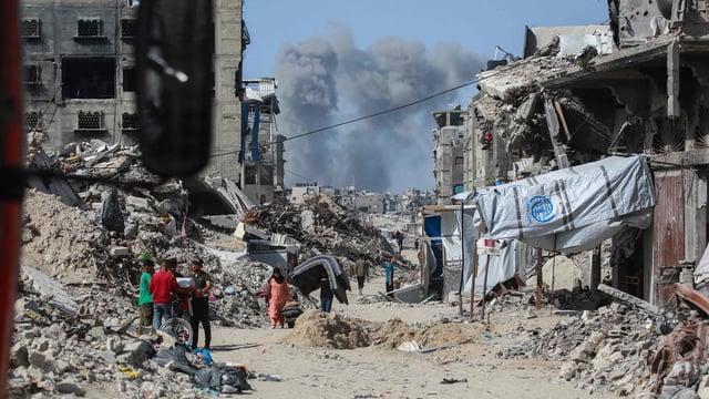 Smoke billows to the north as Palestinians move with their belongings through Jabalia while fleeing the northern Gaza Strip towards Gaza City on May 19, 2025. 