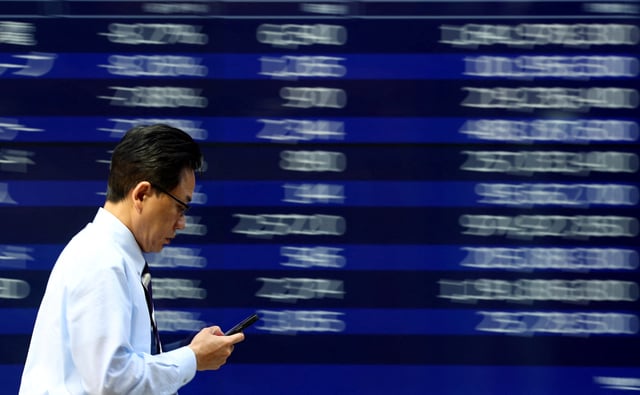 A man walks past an electronic screen displaying stock quotation board in Tokyo, Japan April 15, 2025. REUTERS/Issei Kato/ File Photo