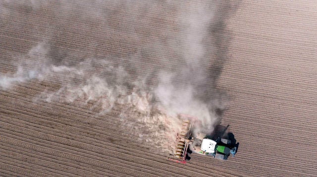 Ein Traktor fährt auf dem Feld und zieht eine Staubwolke hinter sich her.