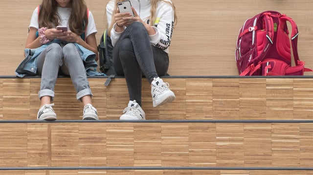 Mädchen sitzen auf einer Stufe und halten Smartphones in den Händen. (Archivbild vom 12.09.2019)