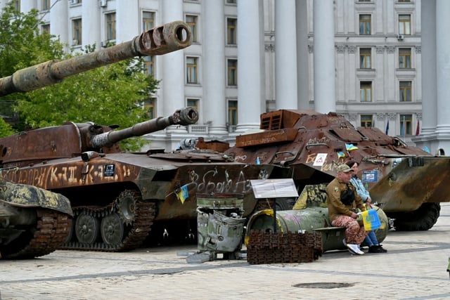 Un volontaire vend des drapeaux ukrainiens, assis sur les débris d'un missile, à Kiev, le 19 mai 2025