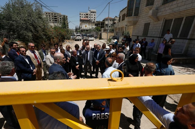 Members of a diplomatic delegation from the European Union stand behind a gate on the eastern entrance of Jenin camp during a visit to the city of Jenin, on May 21, 2025, amid an ongoing Israeli military offensive in the occupied West Bank.
