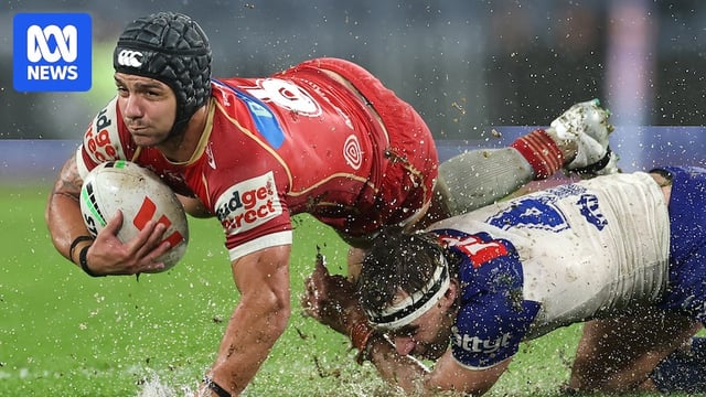 A man tackles another in wet conditions during a rugby league match 