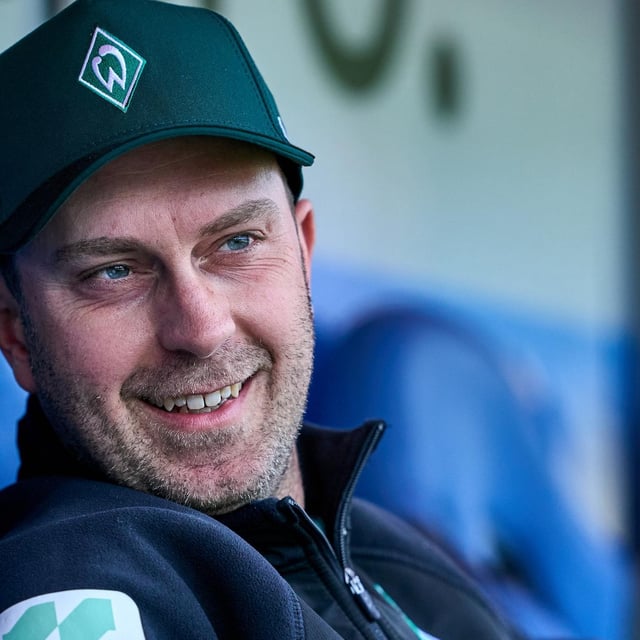 Werder-Trainer Ole Werner sitzt entspannt und lächelnd beim Testspiel gegen Meppen auf der Trainerbank.