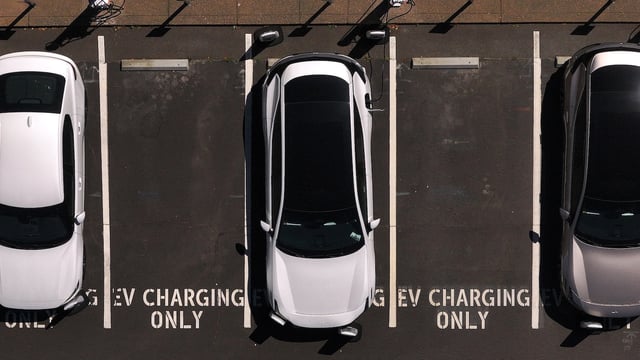 Aerial view of a parking lot with three cars parked. In between them are empty parking spaces with the text "EV charging only" painted in white.