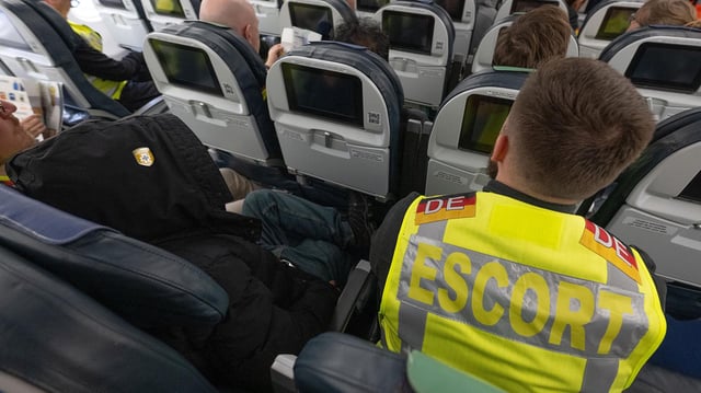 Ein Beamter der Bundespolizei sitzt an Bord eines Abschiebefluges neben einem Mann, der nach Pakistan abgeschoben wird. 