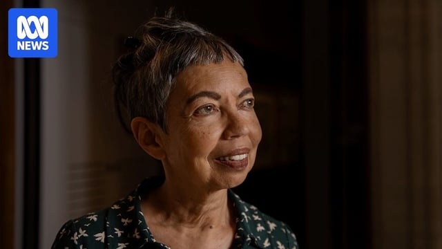 A woman with short greying hair wearing a green patterned shirt gazing to the right with her face tilted upwards