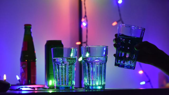 Eine Hand hebt bei einer Party ein Glas von einem Tisch mit weiteren Gläsern und Getränken.