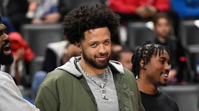 Cunningham smiles toward the camera on the bench at Little Caesars Arena