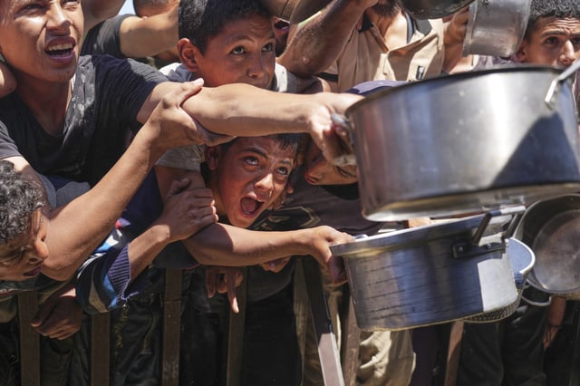 Palestinians struggle to receive cooked food distributed at a community kitchen in the Muwasi area of Khan Younis, in the Gaza Strip, Friday, May 23, 2025. (AP Photo/Abdel Kareem Hana)
