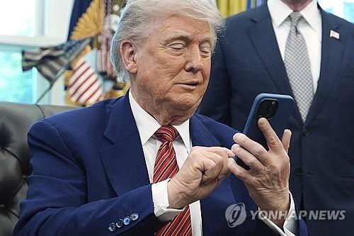 This AP photo shows U.S. President Donald Trump putting his mobile phone on silent, as it rang two times while he was speaking to reporters after signing executive orders in the Oval Office of the White House in Washington, D.C., on May 23, 2025. (PHOTO NOT FOR SALE) (Yonhap)
