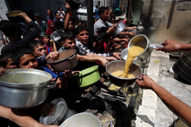Palestinians wait to receive food cooked by a charity kitchen, in Jabalya, in northern Gaza, on May 19, 2025.