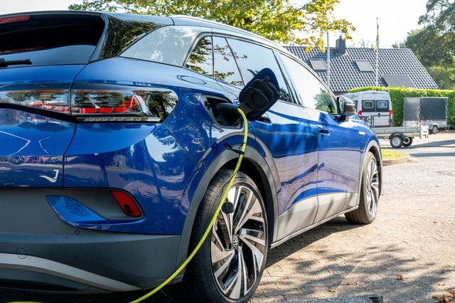 Elektroauto. Ein blaues E-Auto von Volkswagen steht neben einer Ladestation, ein gelbes Ladekabel ragt aus dem Fahrzeug und aus dem Bild heraus