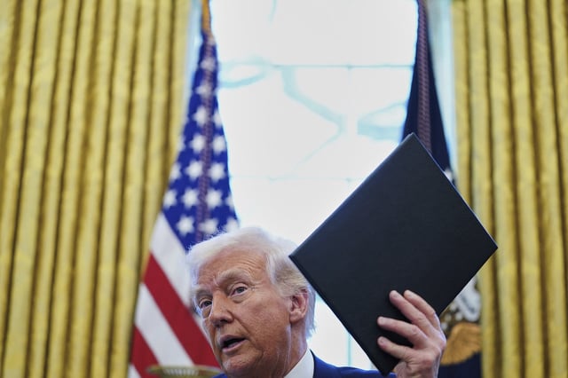 President Donald Trump holds an executive order in the Oval Office of the White House Wednesday, April 9, 2025, in Washington. (Pool via AP)