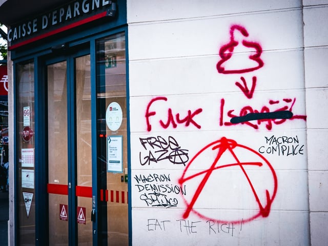 Tag with the inscription Fuck Israel (word Israel crossed out and replaced by a drawing), Macron accomplice, Macron resignation, Free Gaza, letter A surrounded by a circle symbol of the anarchists on the window of a bank the the day after the anti-fascist demonstration in solidarity with Palestine on Sunday June 2, 2024, which ended at Place Gambetta in Paris, France on June 03, 2024. Some damage and numerous tags on walls and windows in solidarity with the Palestinian population, victims of the war between the Israeli army and Hamas (notably in the bombardments in Gaza and Rafah). (Photo by Amaury Cornu / Hans Lucas / Hans Lucas via AFP) (Photo by AMAURY CORNU/Hans Lucas/AFP via Getty Images)