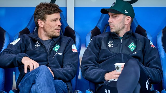 Werder-Trainer Ole Werner und Geschäftsführer Clemens Fritz sitzen vor einem Testspiel nebeneinander auf der blauen Trainerbank und schauen sich im Gespräch an.