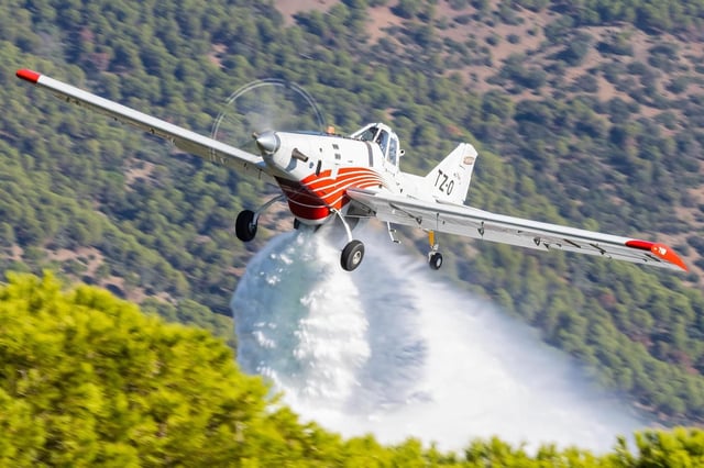 Una avioneta realizando una descarga de agua sobre una zona forestal.