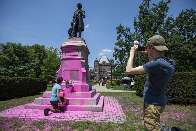 A man places flowers on a statue of Sir John A. Macdonald after demonstrators threw pink paint on it at Queen’s Park in Toronto on Saturday, July 18, 2020. The man said it was disappointing to see the statue vandalized and the flower were to show his respect to Sir John A. Macdonald.THE CANADIAN PRESS/Carlos Osorio