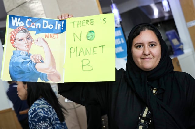 A woman holds up a sign  during a demonstration calling for a stand against climate change in Qatar, a country where climate change is making certain cancers more common and more deadly among women.