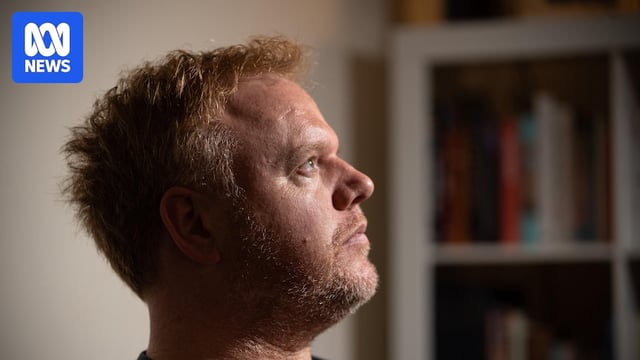 A man looks to up, to the side and out of frame with a serious expression.