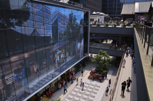 People tour by a projector screen promoting a newly opened outdoor Hutong style shopping mall, in Beijing, Monday, May 26, 2025. (AP Photo/Andy Wong)