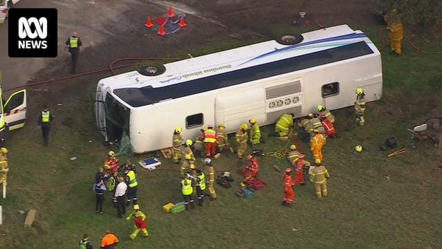 A white bus on its side surrounded by emergency services personnel in high vis.