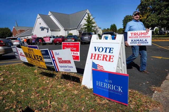 A supporter for then-former President Donald Trump walks past political signs outside the Rutherford County Annex Building, an early voting site in October 2024 in Rutherfordton, North Carolina. (KATHY KMONICEK/AP FILE)