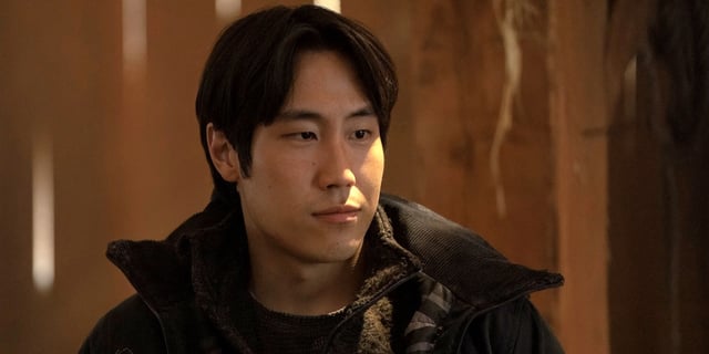 Young Mazino as Jesse looking off to the left in a black coat in The Last of Us Season 2