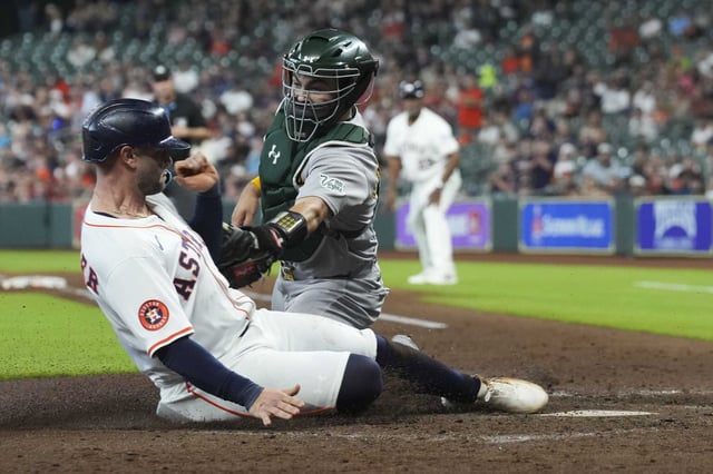 Houston Astros Christian Walker (8) slides under the tag of Athletics catcher Shea Langeliers to score on Cam Smith’s RBI single in the fourth inning of an MLB baseball game in Houston, Wednesday, May 28, 2025.