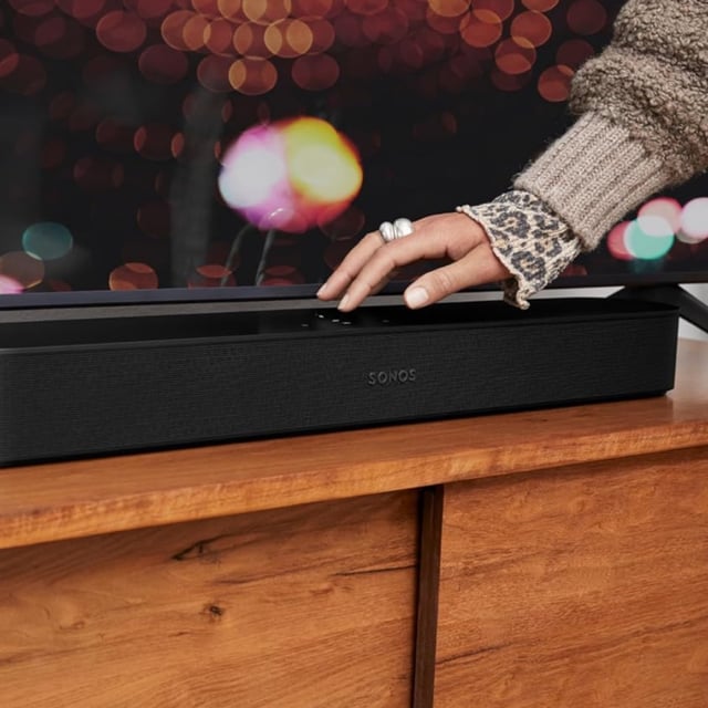person touching Sonos Beam soundbar that sits in front of TV
