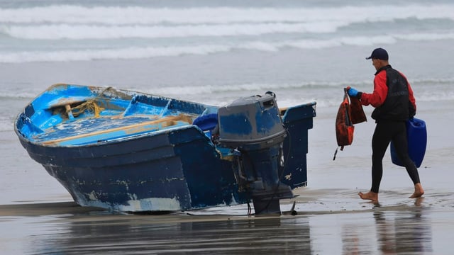 A Del Mar lifeguard gathers debris such as lifejackets and gas cans as they worked to secure the scene where a suspected smuggling panga overturned in the surf in Del Mar early Monday. Three people were confirmed dead and a number of people were unaccounted for. (K.C. Alfred / The San Diego Union-Tribune)