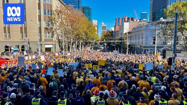 A huge crowd of people holding a protest in a city CBD beneath a clear sky.