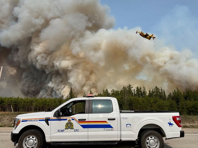 A Royal Canadian Mounted Police (RCMP) patrol vehicle is parked as a water bomber flies over the plume of smoke from a wildfire near The Pas, Manitoba, Canada May 27, 2025. Manitoba RCMP/Handout via REUTERS