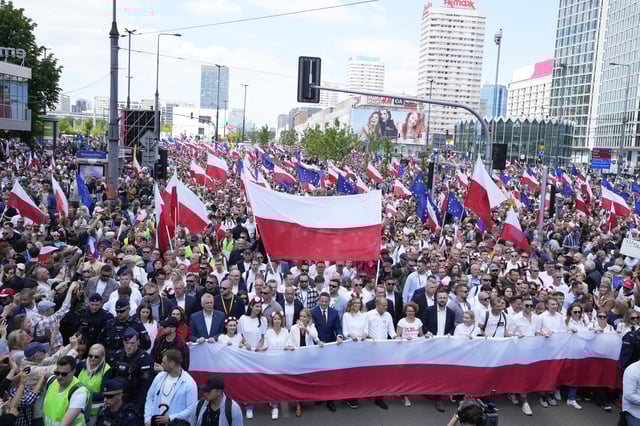The liberal presidential candidate Rafal Trzaskowski holds a giant polish flag in the first row as he stands next to a waving women during a march one week ahead of a decisive presidential election in Warsaw, Poland on Sunday, May 25, 2025. (AP Photo/Czarek Sokolowski)