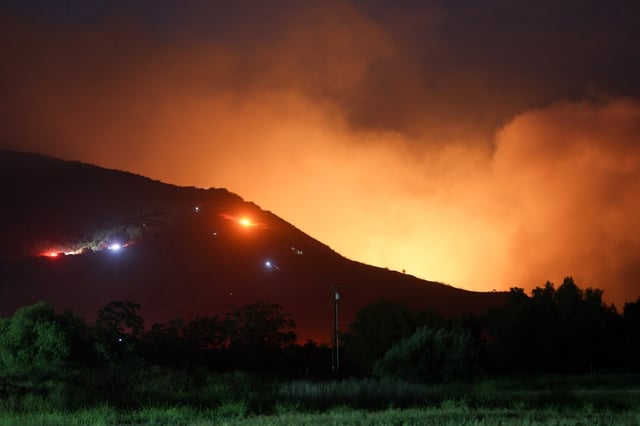 Fire trucks can be seen next to a brushfire burning in Pala on Friday, May 30, 2025. (Hayne Palmour IV / For The San Diego Union-Tribune)