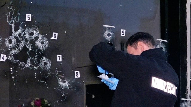 Ein Polizist sichert Spuren an der zerschossenen Schaufensterscheibe.