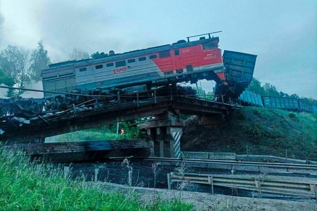 Eine zerstörte Brücke mit aufsteigendem Rauch, darauf ein Teil eines Zugs.