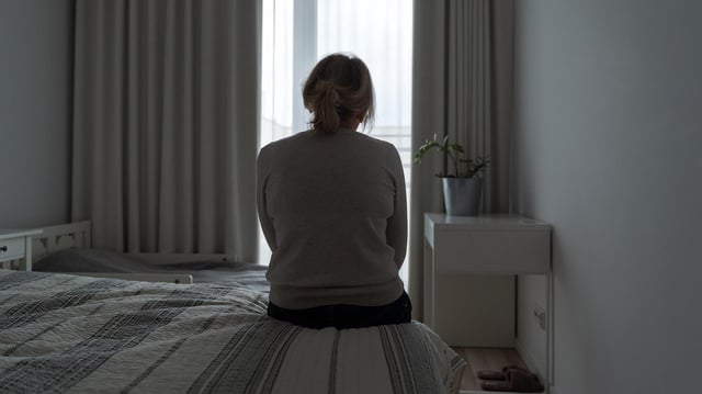 Eine Frau sitzt auf einem Bett und blickt aus dem Fenster.