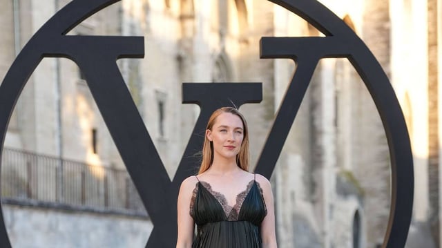 AVIGNON, FRANCE - MAY 22: Saoirse Ronan wears a black pleated low-neck dress with dark green hue featuring delicate lace trim and thin straps. Hair is styled straight and parted in the center. Black sandals complete the look, outside Louis Vuitton, during the Louis Vuitton Cruise 2026 at Palais Des Papes, on May 22, 2025 in Avignon, France. (Photo by Edward Berthelot/Getty Images)