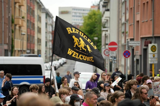 Menschen protestieren mit einer schwarz-gelben Fahne auf "Refugees are welcome" zu lesen ist