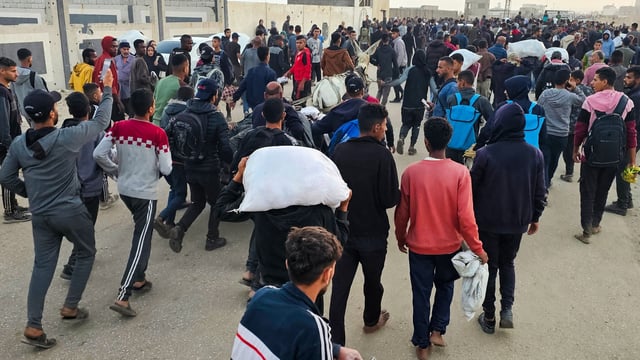 Displaced Palestinians, some carrying sacks of food, leave a distribution centre in Rafah, 