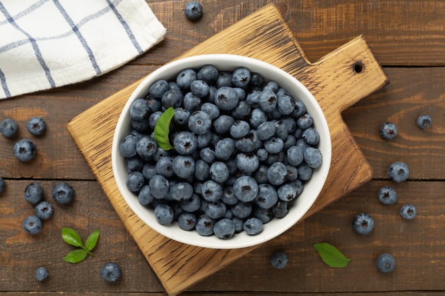 A bowl of blueberries is laid out on a wooden table.