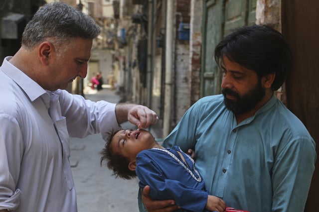A health worker, left, administers a polio vaccine to a child at a neighborhood in Peshawar, Pakistan, Monday, May 26, 2025. (AP Photo/Muhammad Sajjad)