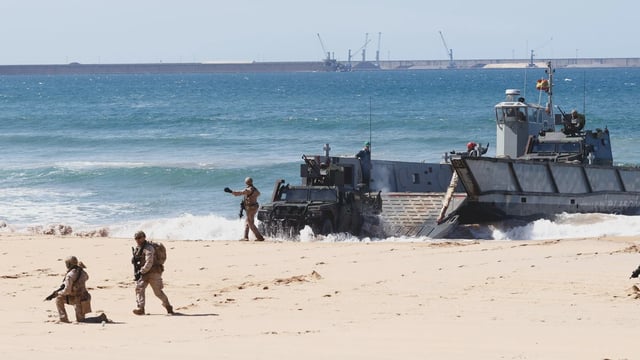 Vehículos y militares salen de una de las lanchas de desembarco de la Armada en la playa de Gijón