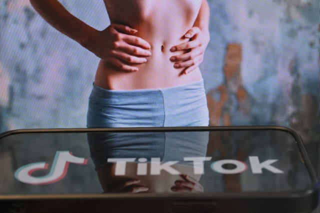 Photo d'illustration du 7 mai 2025 montrant le logo de Tik Tok sur un smartphone devant un écran affichant l'image d'une femme très mince, alors que la tendance "skinnytok" promouvant la minceur inquiète les experts