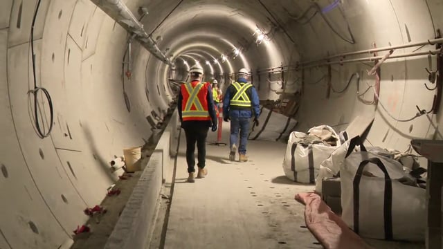 Two people walk in the partly constructed Broadway subway tunnels.