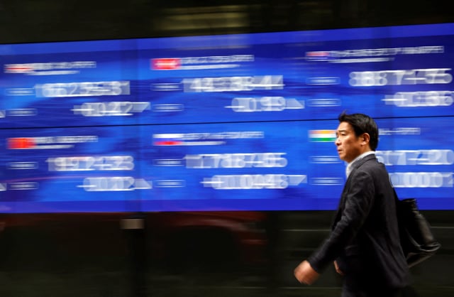 A passerby walks past an electric monitor displaying various countries' stock price index outside a bank in Tokyo, Japan, March 22, 2023. REUTERS/Issei Kato/File Photo