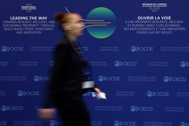 A woman walks past a poster with the OECD logos before the launch of the OECD Economic Outlook and the 2025 Ministerial Council Meeting at the OECD Headquarters in Paris, France, June 3, 2025. REUTERS/Benoit Tessier